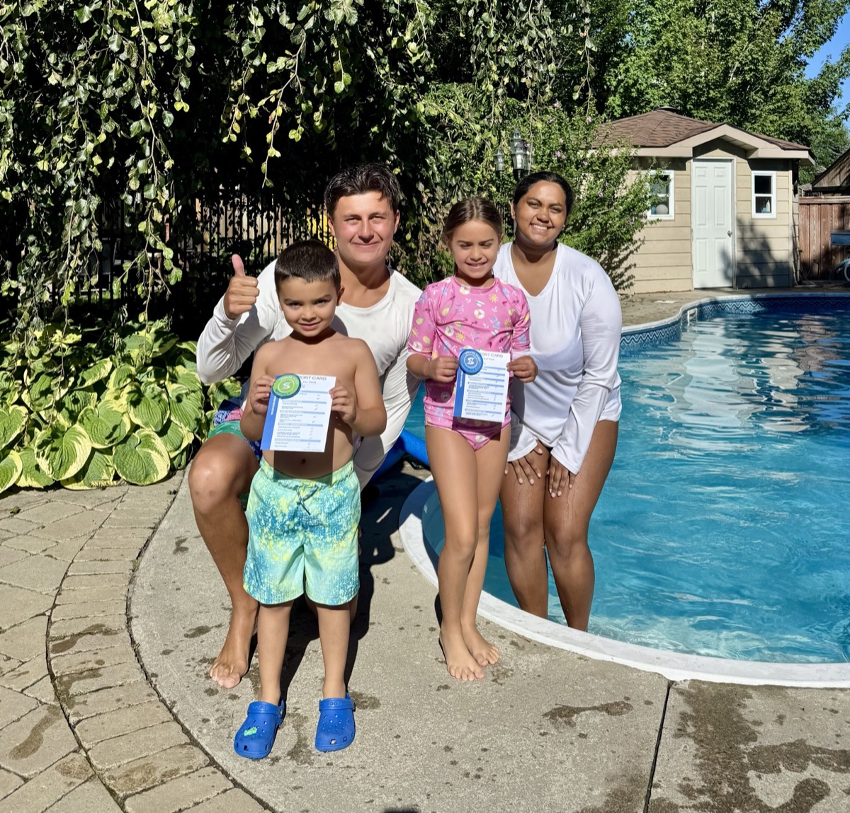 Two young swimmers holding their progress cards with Ilios instructors beside the pool